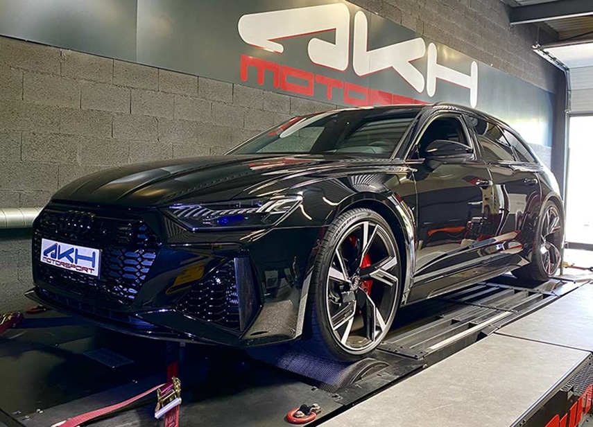 Audi RS6 : Tests performance sur banc chez AKH Motorsport Audi RS6 noire sur un banc de puissance, avec le logo AKH Motorsport visible sur le pare-chocs et sur le mur en arrière-plan.