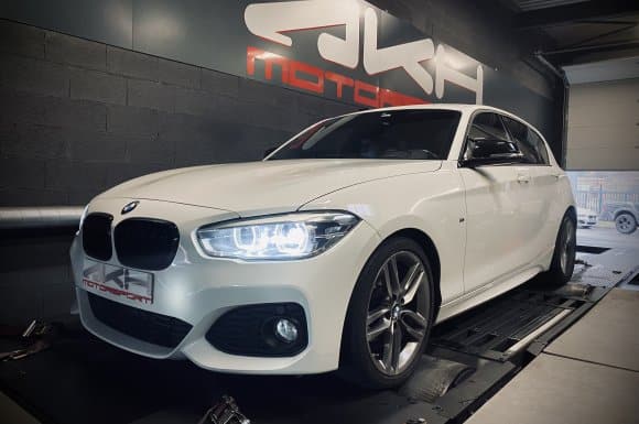 BMW Série 1 blanche sur banc de puissance chez JKF Motorsport. Phares allumés, prête pour l'optimisation moteur.
