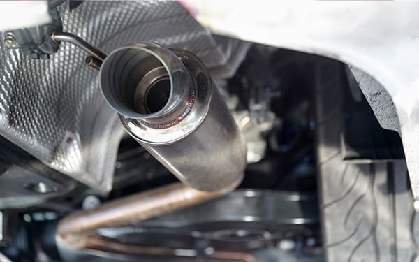 Pot d'échappement sport en titane ou acier inoxydable sous une voiture, avec soudures colorées et bouclier thermique. Vue de dessous.