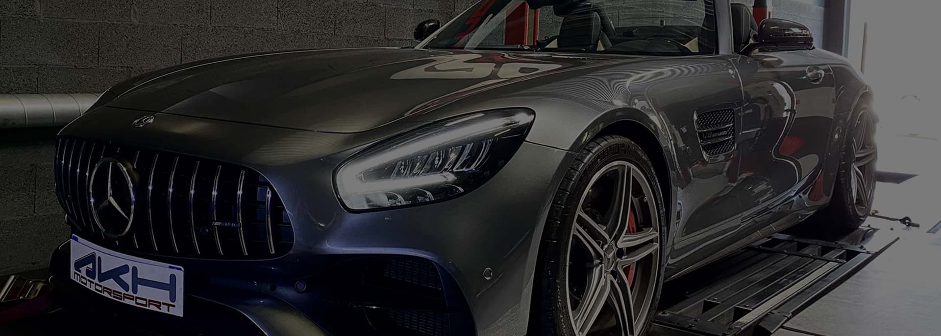 Mercedes-Benz AMG GT gris sur banc de puissance. Phares allumés, plaque AKH MOTORSPORT, badge V8 BITURBO.
