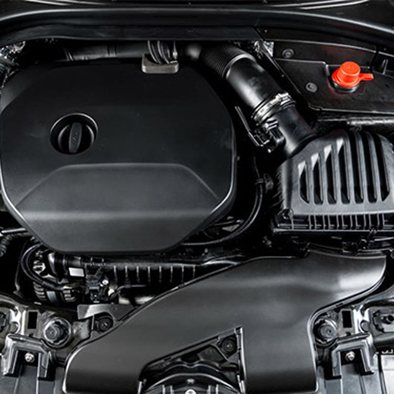 Compartiment moteur de voiture moderne, affichant le cache noir, le système d'admission d'air et une borne rouge.