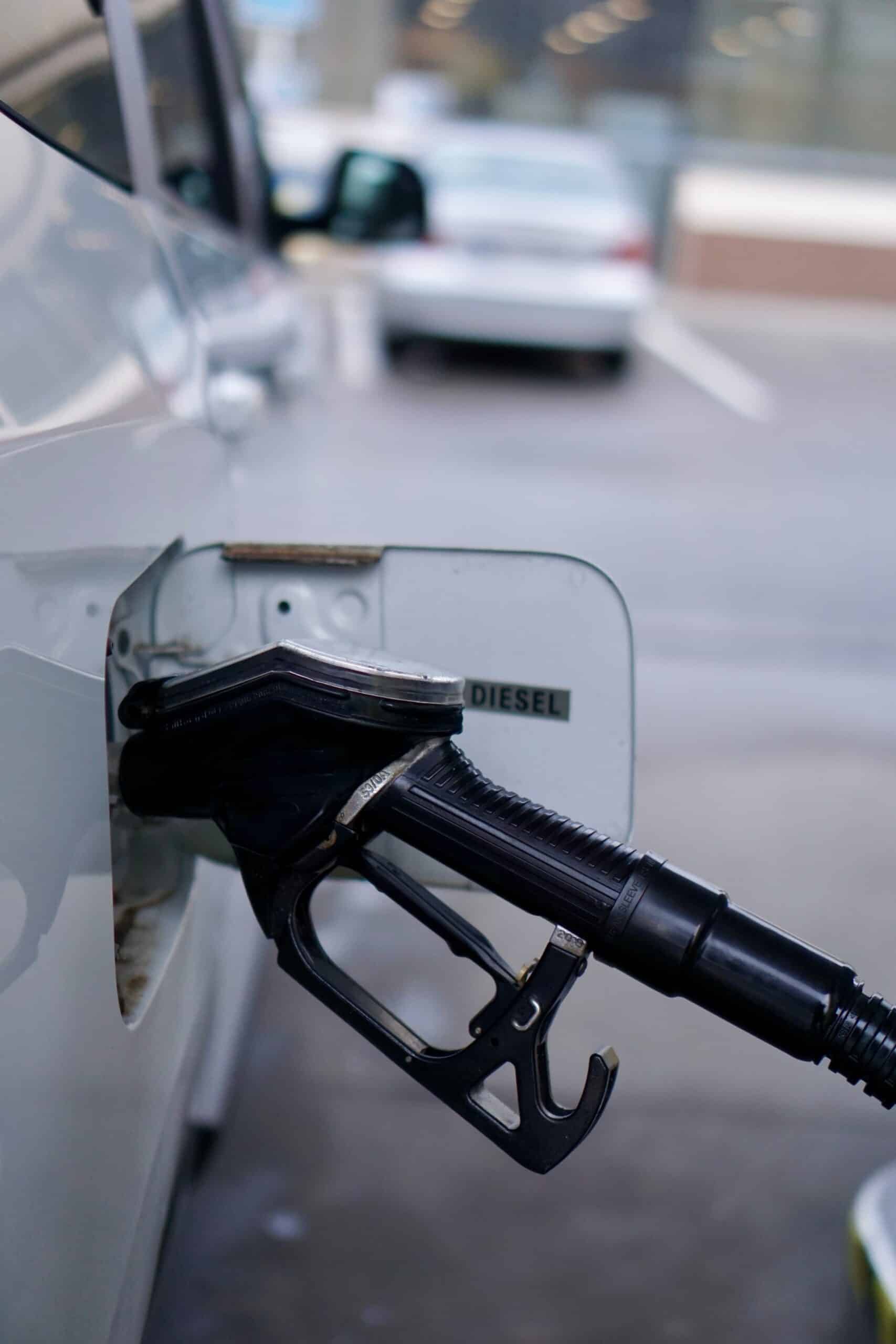 Buse de carburant DIESEL noire insérée dans le réservoir d'une voiture blanche. Le volet indique "DIESEL".