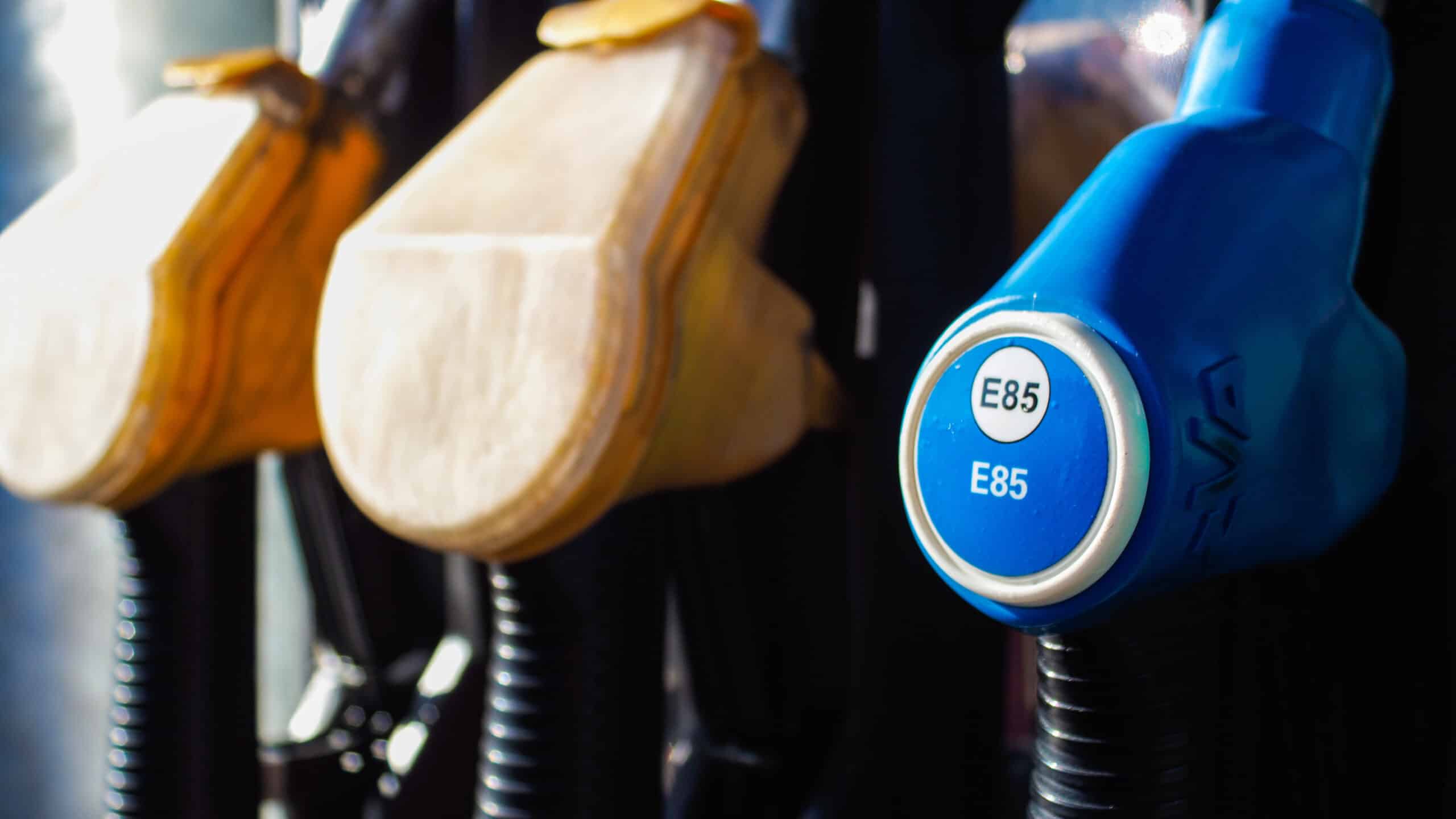 Buse de pompe à carburant E85 bleue en gros plan, affichant 'E85', avec deux buses jaunes floues derrière.