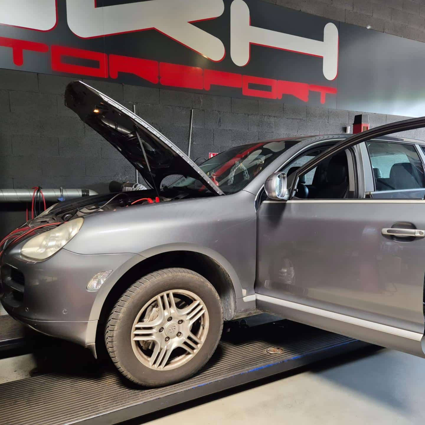 Porsche Cayenne gris sur banc de puissance TRH TORQUE, capot ouvert pour optimisation moteur. Câblage visible, porte conducteur ouverte.