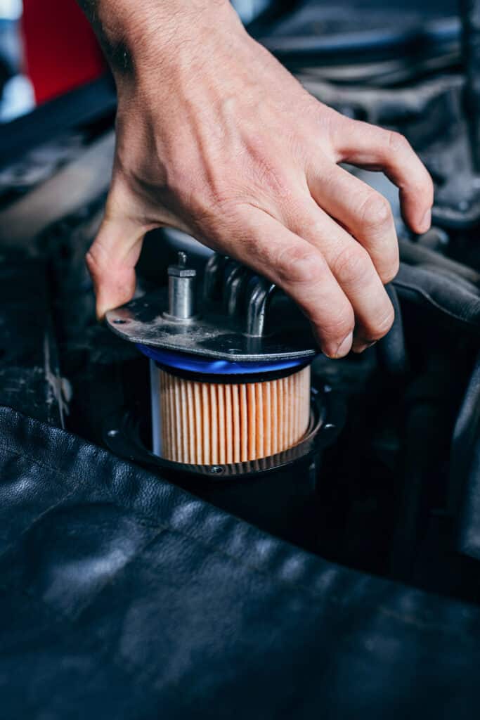 Remplacement Filtre Moteur Voiture - Entretien Auto Main tenant un filtre de moteur strié lors d'un entretien de voiture. Le filtre est inséré dans le compartiment moteur.