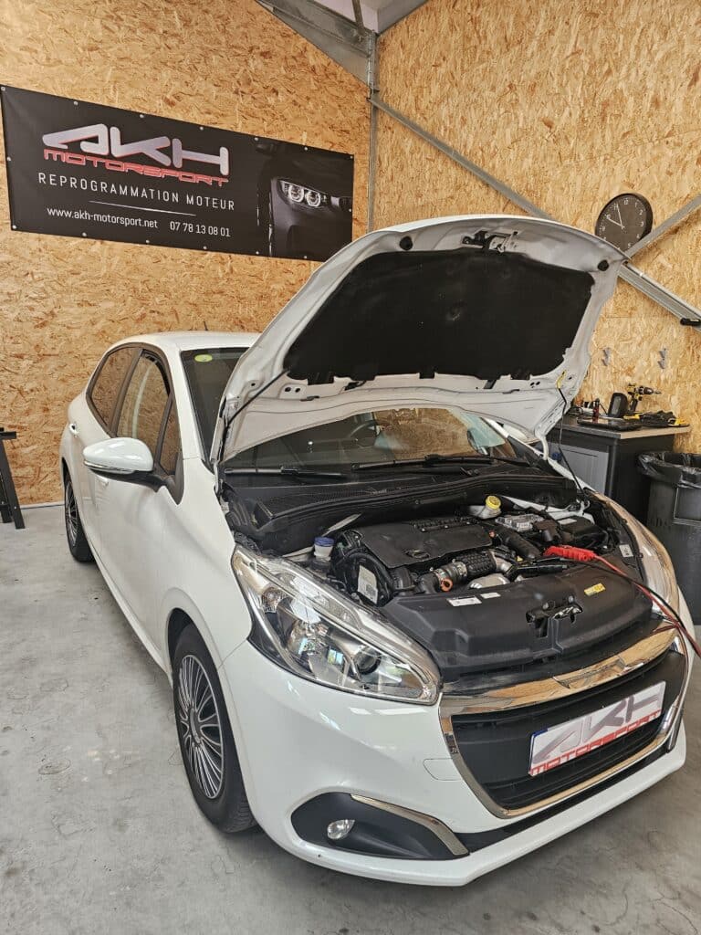 Reprogrammation Moteur AKH Motorsport: Peugeot 208 Peugeot 208 blanche, capot ouvert, en reprogrammation moteur chez AKH Motorsport dans un atelier. Outils visibles.