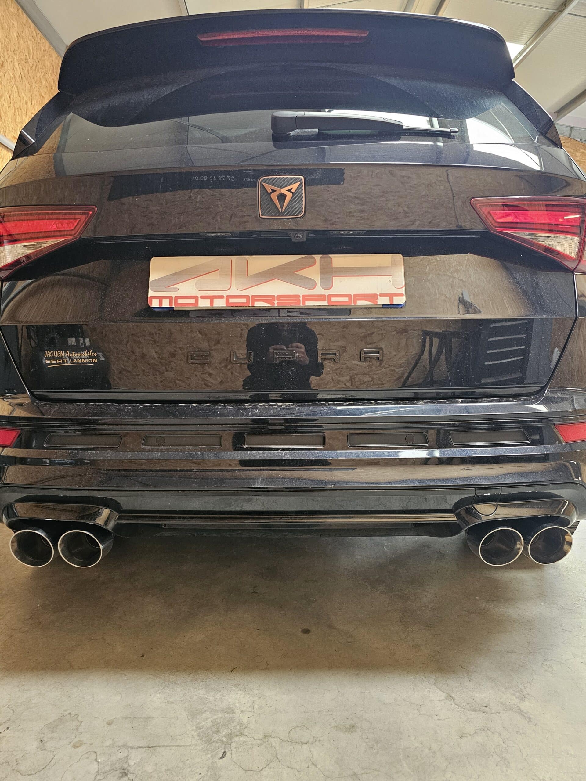Arrière d'une Cupra noire avec logo bronze, plaque AKH Motorsport et quatre sorties d'échappement sportives.