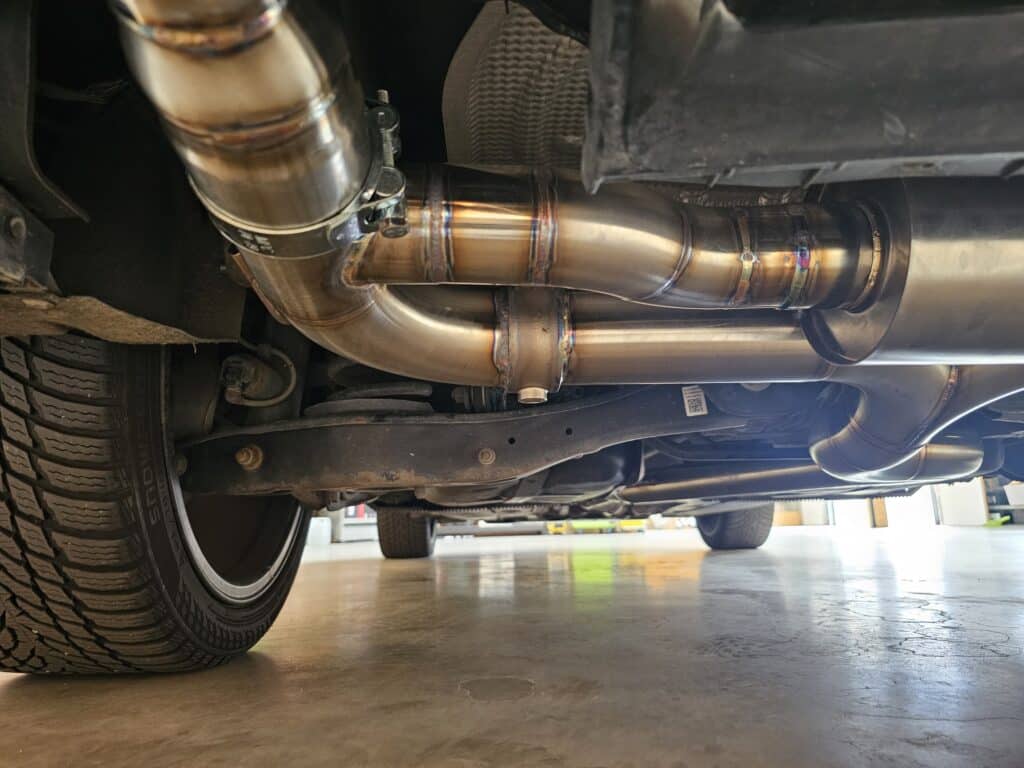Ligne d'échappement custom inox sous voiture. Magnifiques soudures TIG, colliers V-band, et suspension arrière. Pneu SNOWBLADE visible.