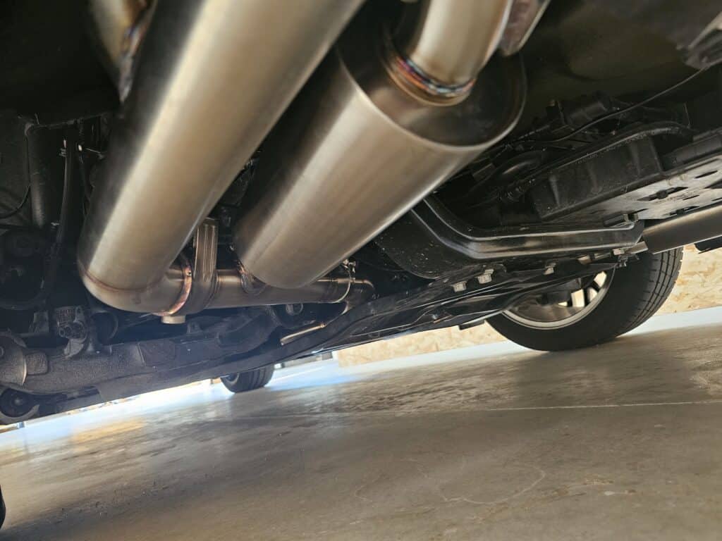 Échappement inox haute performance sous châssis voiture Vue du système d'échappement inox sous un châssis automobile avec tuyaux soudés et résonateur haute performance.