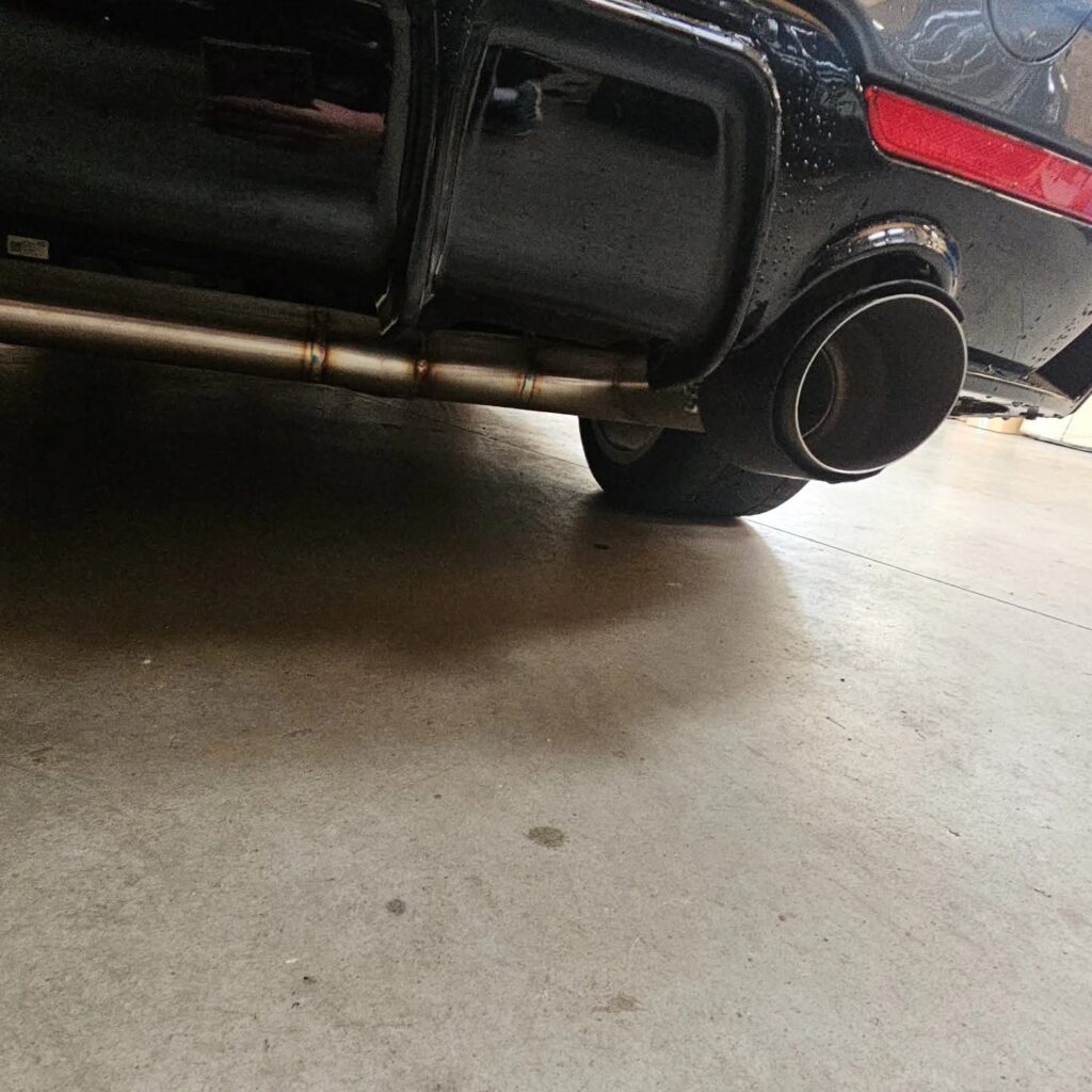 Pot d'échappement sport en inox pour voiture personnalisée Zoom sur un pot d'échappement sport en acier avec soudures visibles sur l'arrière d'une voiture noire.