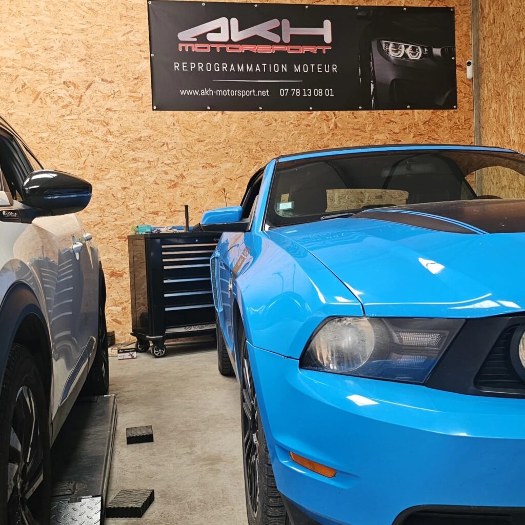 Reprogrammation Moteur Mustang - Expertise AKH Motorsport Ford Mustang bleue chez AKH Motorsport pour une reprogrammation moteur, avec bannière et coordonnées visibles.