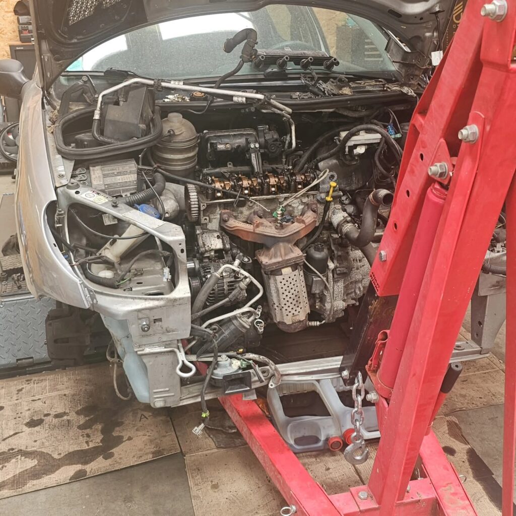 Démontage moteur voiture avec grue d'atelier rouge Moteur exposé et palan rouge lors d'un démontage mécanique dans un atelier.