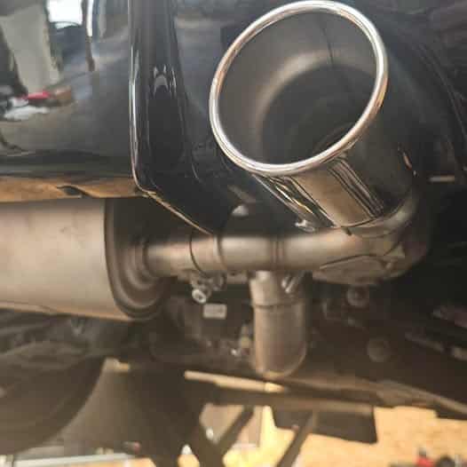 Échappement Sport Chrome : Vue du Silencieux sous la Voiture Sortie d'échappement en chrome poli et silencieux sous une voiture sur un pont de garage.